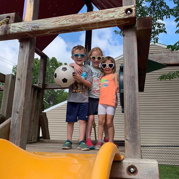 kids standing at the top of a swing set with sunglasses on and a soccer ball in hands