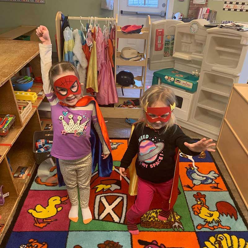 kids dressing up as superheroes, both have red masks on and one has her fist up in the air, the other has her arm forward